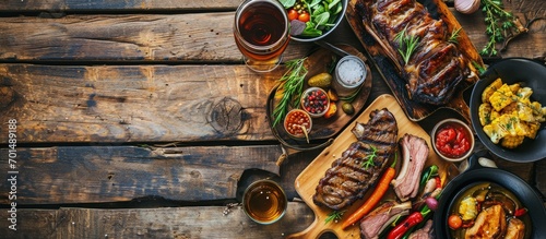 Wooden table served with various grilled meat vegetables and glasses of beer Striploin steak ribeye steak and lamb ribs on wooden cutting boards Top view. Creative Banner. Copyspace image photo