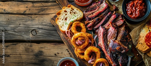 Traditional smoked barbecue wagyu beef brisket offered with farmhouse bread as top view on an old cutting board with Louisiana sauce onion rings and peperoni. Creative Banner. Copyspace image photo