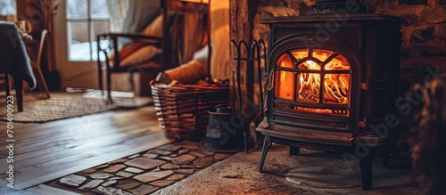 Fotografija Vertical photo of wood stove fireplace with fire in metal body and glass door Wicker basket in comfort house with cozy interior in warm room