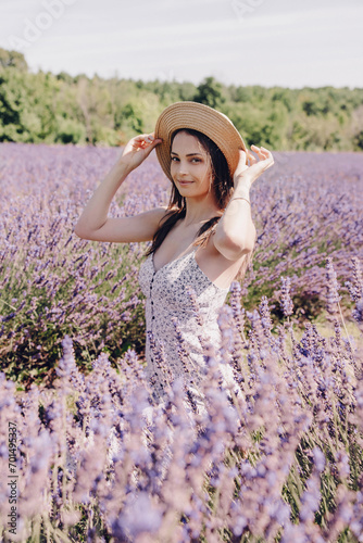 Beautiful young woman in the middle of a blooming lavender field. Young brunette in a straw hat at a lavender farm in Provence. Beautiful purple lavender field. Vertical portrait of a posing woman © halcon1