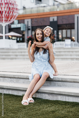 A young mother and her daughter are having fun outdoors. Mom and daughter, dressed in summer dresses, are having fun and hugging. Happy childhood and motherhood