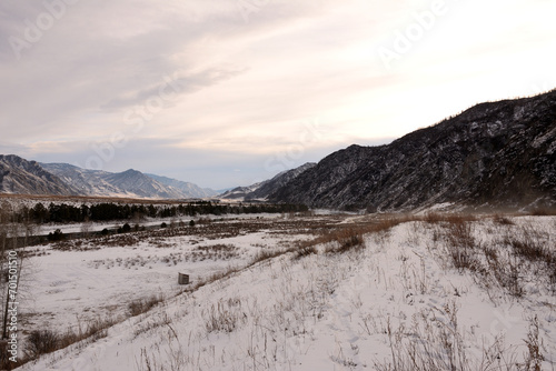 Fotografi The sloping high bank of a beautiful ice-bound river with clearings at the foot of high mountains covered with snow