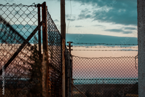 Barbed iron wire against blue sky. Industrial zone protected with a lattice fence. Warehouse, factory territory. Private property. Jail, prison zone.