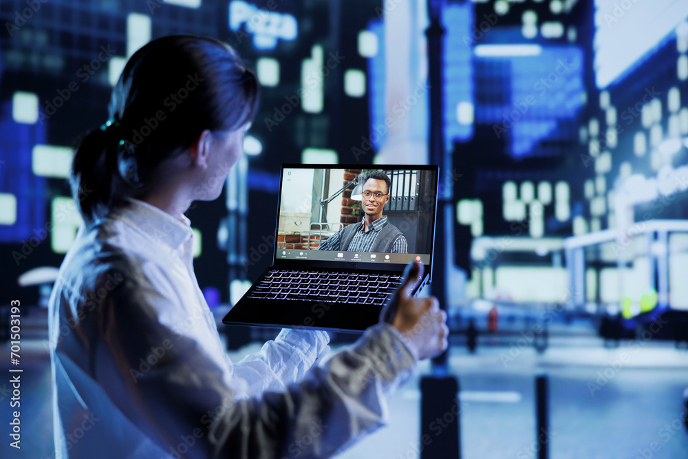Asian man in videocall with coworker using device while strolling around city streets at night, giving him work updates. Person uses laptop to show colleague surroundings in illuminated urban district Asian man in videocall with coworker using device while strolling around city streets at night, giving him work updates. Person uses laptop to show colleague surroundings in illuminated urban district
