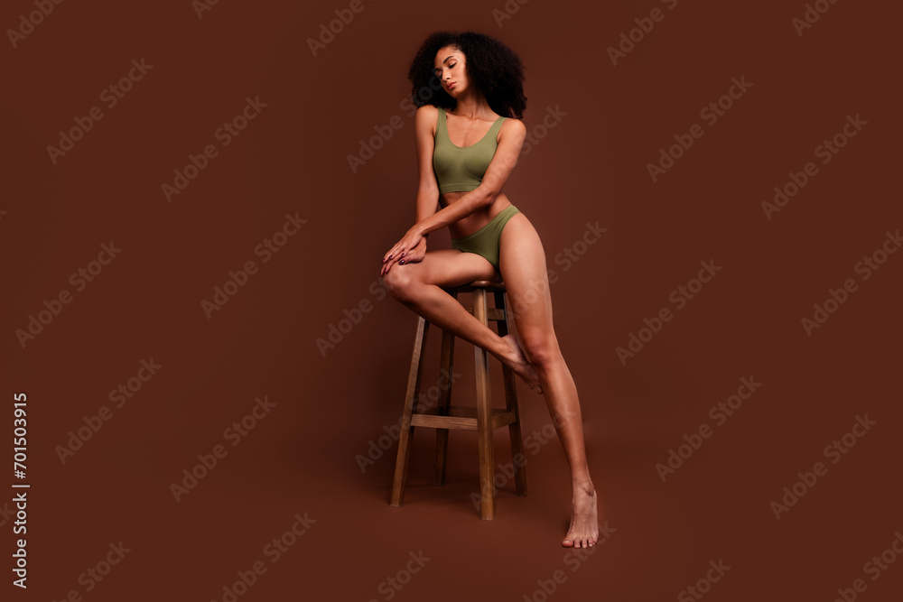 No filter photo of stunning woman athlete with sporty muscular body sitting stool isolated on brown color background