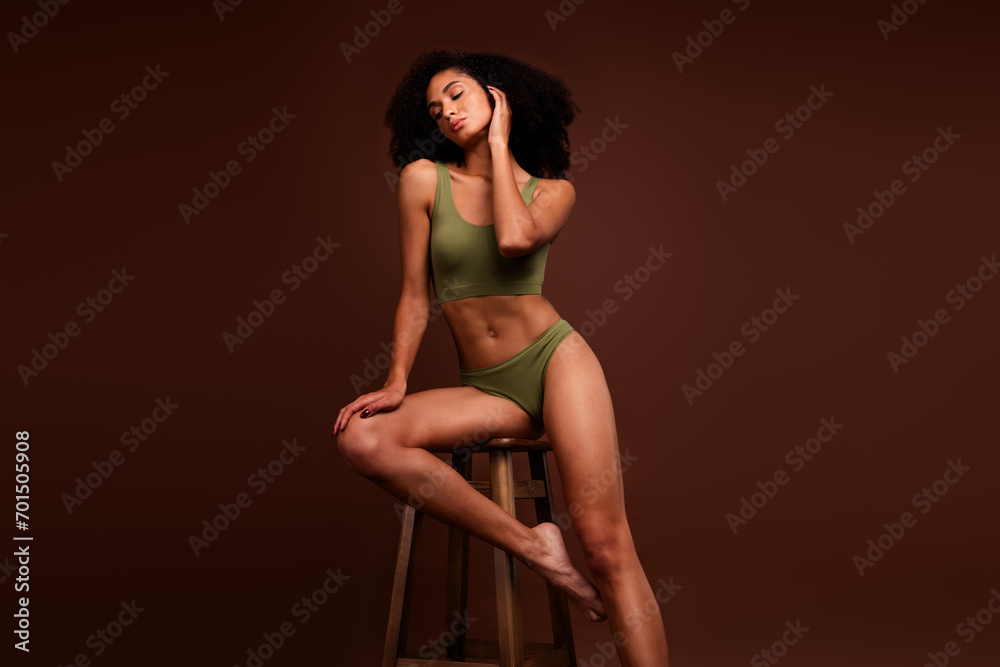 No filter photo of gorgeous woman tank top and panties strong sporty body posing on stool isolated over brown color background