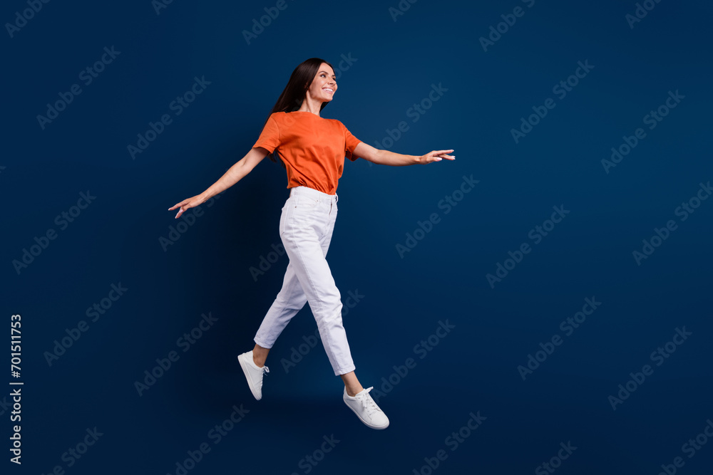 Full length photo of funky pretty woman dressed orange t-shirt jumping high walking empty space isolated dark blue color background