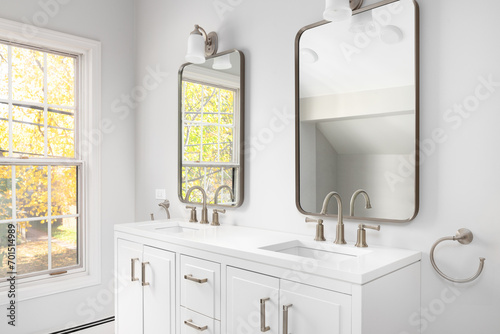 A bathroom detail with a white cabinet, bronze faucets and mirrors, and colorful trees out the windows.