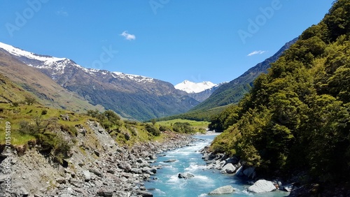 New zealand river blue water with green rocks and mountains with snow blue sky