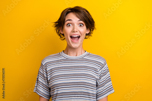 Portrait of impressed overjoyed girl with short hairstyle wear grey t-shirt astonihsed staring isolated on yellow color background