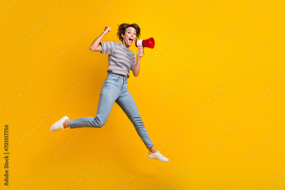 Full size photo of delighted nice girl jump raise fist hold loudspeaker empty space isolated on yellow color background