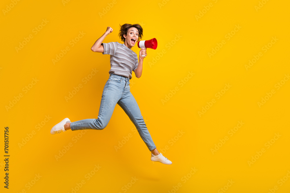 Full size photo of delighted nice girl jump raise fist hold loudspeaker empty space isolated on yellow color background Full size photo of delighted nice girl jump raise fist hold loudspeaker empty space isolated on yellow color background