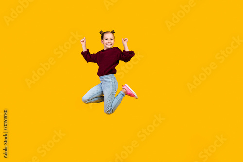 Full body portrait of overjoyed small schoolkid jumping raise fists empty space isolated on yellow color background © deagreez