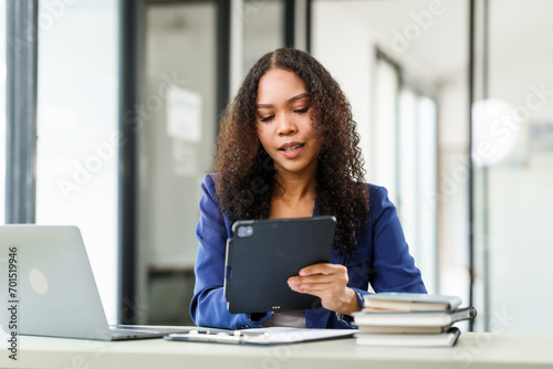 African American university woman working on a project, using a laptop and taking notes, looking focused and engaged.