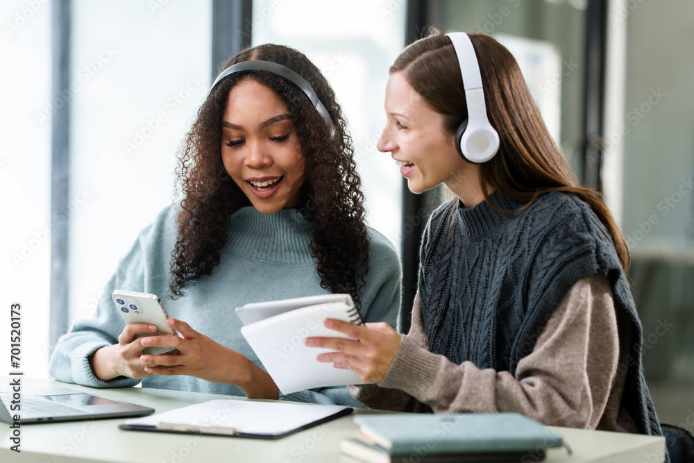 Caucasian and an African American university woman working together on a project, discussing and taking notes. Caucasian and an African American university woman working together on a project, discussing and taking notes.