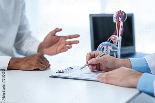 close-up of male patient consultation with doctor, explaining model of reproductive system, possibly discussing prostate cancer, cystitis, or urinary tract infection. photo