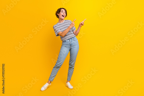 Full size photo of astonished cute girl look direct fingers empty space ad isolated on yellow color background