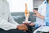 male patient and male doctor discussing a model of a knee joint, likely focusing on condition of knee arthritis during a medical consultation.