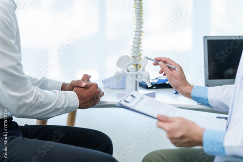 Close up male doctor and patient people in a medical office, spine model, possibly discussing spinal condition or syndrome with the patient.
