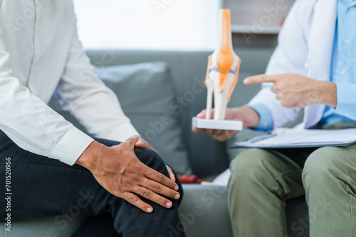Doctor is seeing a patient. sitting and holding his knees with discomfort Meanwhile, bone model. talking about knee pain or osteoarthritis. photo