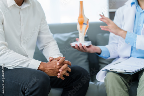 male patient and male doctor discussing a model of a knee joint, likely focusing on condition of knee arthritis during a medical consultation. photo
