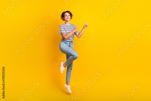 Fototapet Full size photo of nice cheerful girl jumping indicate fingers empty space propo