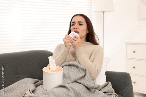 Sick woman with tissue sneezing on sofa at home. Cold symptoms
