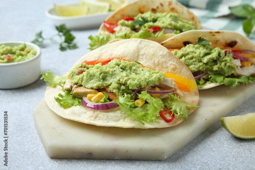 Delicious tacos with guacamole, meat and vegetables on light grey table, closeup
