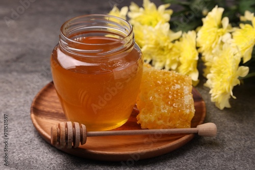 Sweet golden honey in jar, dipper and honeycomb on grey textured table, closeup