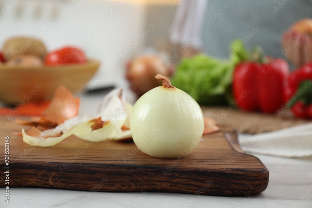 Wooden board with fresh onion and peels on white marble table, closeup Wooden board with fresh onion and peels on white marble table, closeup