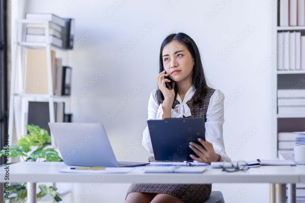 Asian woman entrepreneur busy with her work in the office. Young Asian woman work on desk laptop phone while planning sales, research or financial strategy in company Asian woman entrepreneur busy with her work in the office. Young Asian woman work on desk laptop phone while planning sales, research or financial strategy in company