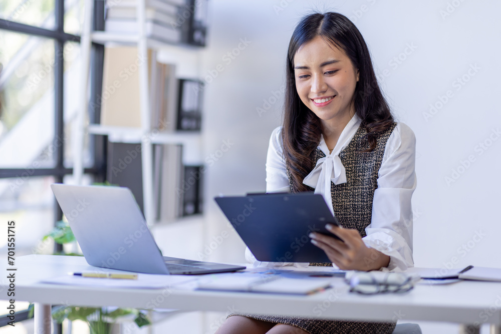 Asian woman entrepreneur busy with her work in the office. Young Asian woman work on desk laptop phone while planning sales, research or financial strategy in company Asian woman entrepreneur busy with her work in the office. Young Asian woman work on desk laptop phone while planning sales, research or financial strategy in company