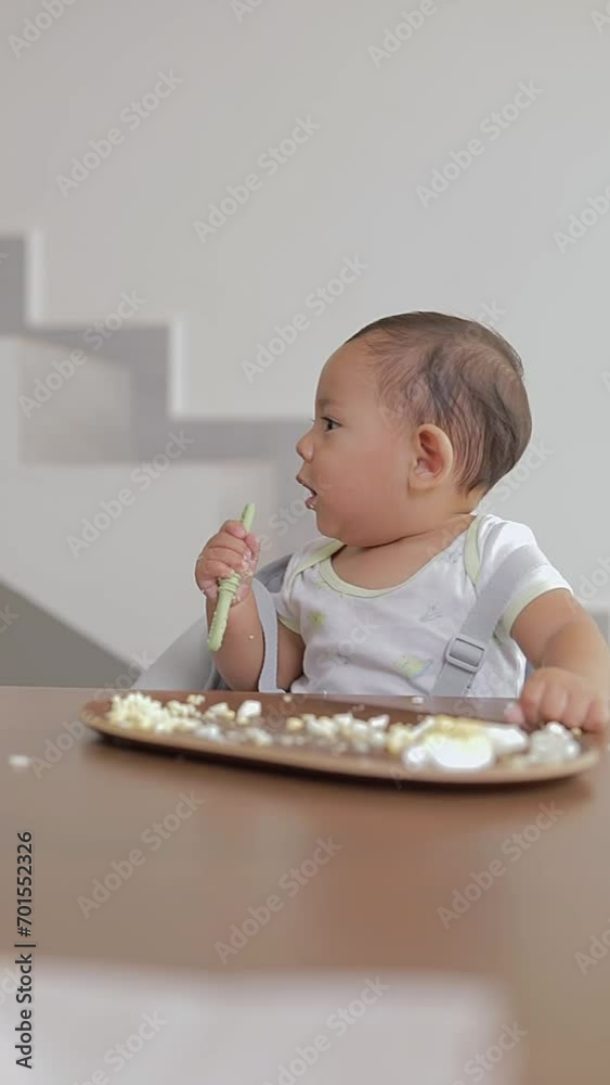 Latino baby chewing on a spoon while eating while sitting at a table Latino baby chewing on a spoon while eating while sitting at a table