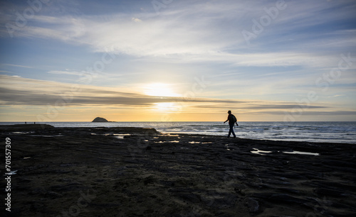 Obraz na płótnie Man walking on the rocks at sunset at Muriwai beach. Oaia Island in the distance. Auckland. w salonie