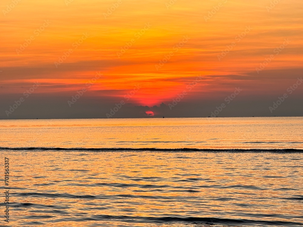 Sun going down in orange sky over horizon. Golden sunset at the sea with soft waves. Tropical sunset. Seascape and shore.
