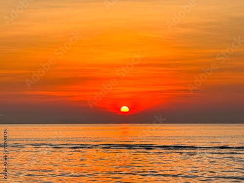 Fototapeta Naklejka Na Ścianę i Meble -  Sun going down in orange sky over horizon. Golden sunset at the sea with soft waves. Tropical sunset. Seascape and shore.

