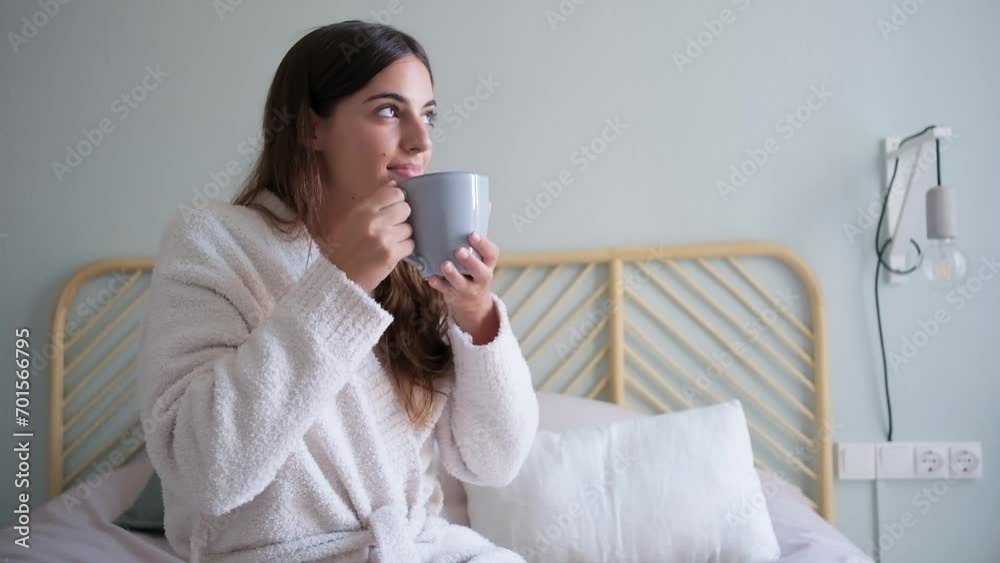 Pensive happy young caucasian woman sitting on bed looking out the window holding coffee cup with hands. HD video. Pensive happy young caucasian woman sitting on bed looking out the window holding coffee cup with hands. HD video.