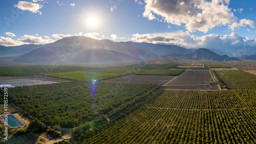 Aerial view of fields with mountains in the distance and sun rays coming through the clouds.
