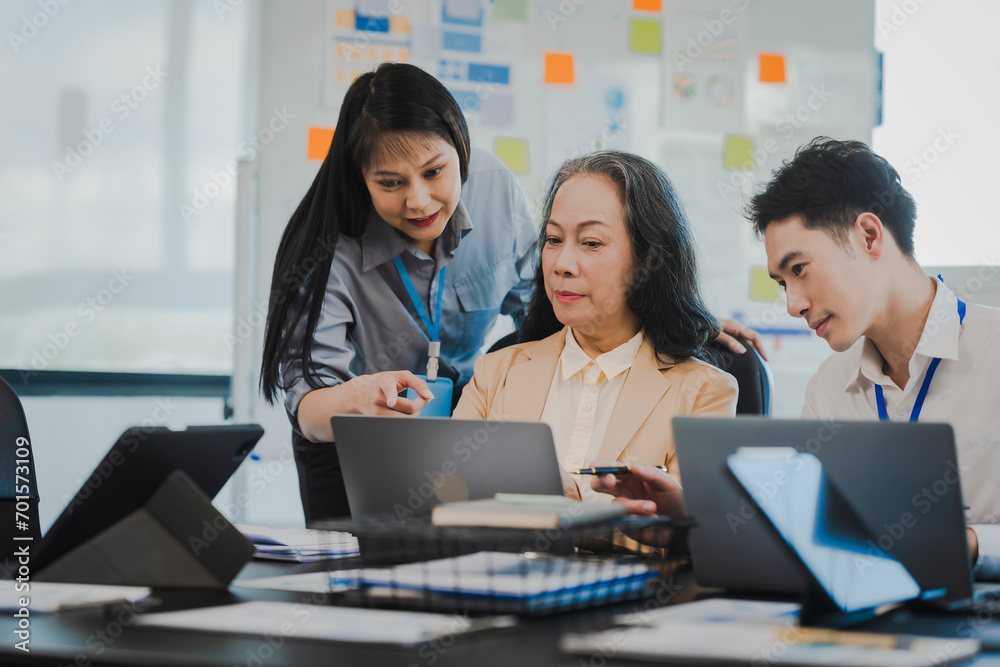 Asian office worker discussing with younger colleagues over laptops in a meeting room, possibly reviewing monthly reports or sharing opinions. Asian office worker discussing with younger colleagues over laptops in a meeting room, possibly reviewing monthly reports or sharing opinions.