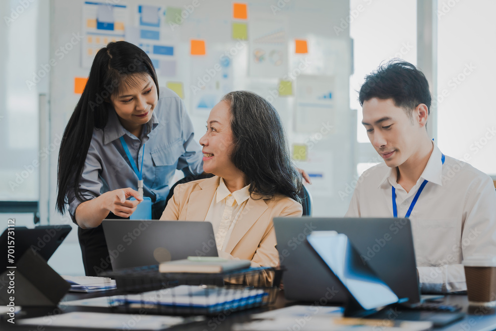 Asian office worker discussing with younger colleagues over laptops in a meeting room, possibly reviewing monthly reports or sharing opinions. Asian office worker discussing with younger colleagues over laptops in a meeting room, possibly reviewing monthly reports or sharing opinions.