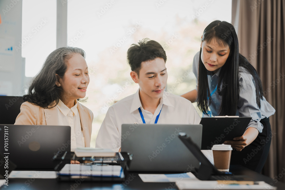 Asian office worker discussing with younger colleagues over laptops in a meeting room, possibly reviewing monthly reports or sharing opinions. Asian office worker discussing with younger colleagues over laptops in a meeting room, possibly reviewing monthly reports or sharing opinions.