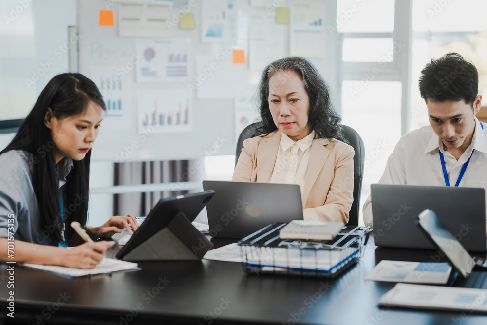 Asian office worker discussing with younger colleagues over laptops in a meeting room, possibly reviewing monthly reports or sharing opinions. Asian office worker discussing with younger colleagues over laptops in a meeting room, possibly reviewing monthly reports or sharing opinions.