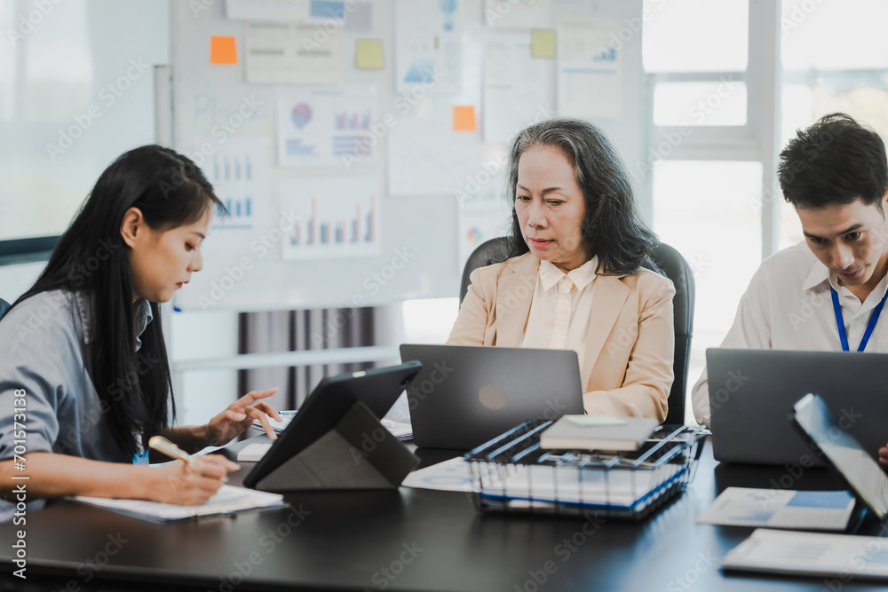 Asian office worker discussing with younger colleagues over laptops in a meeting room, possibly reviewing monthly reports or sharing opinions. Asian office worker discussing with younger colleagues over laptops in a meeting room, possibly reviewing monthly reports or sharing opinions.
