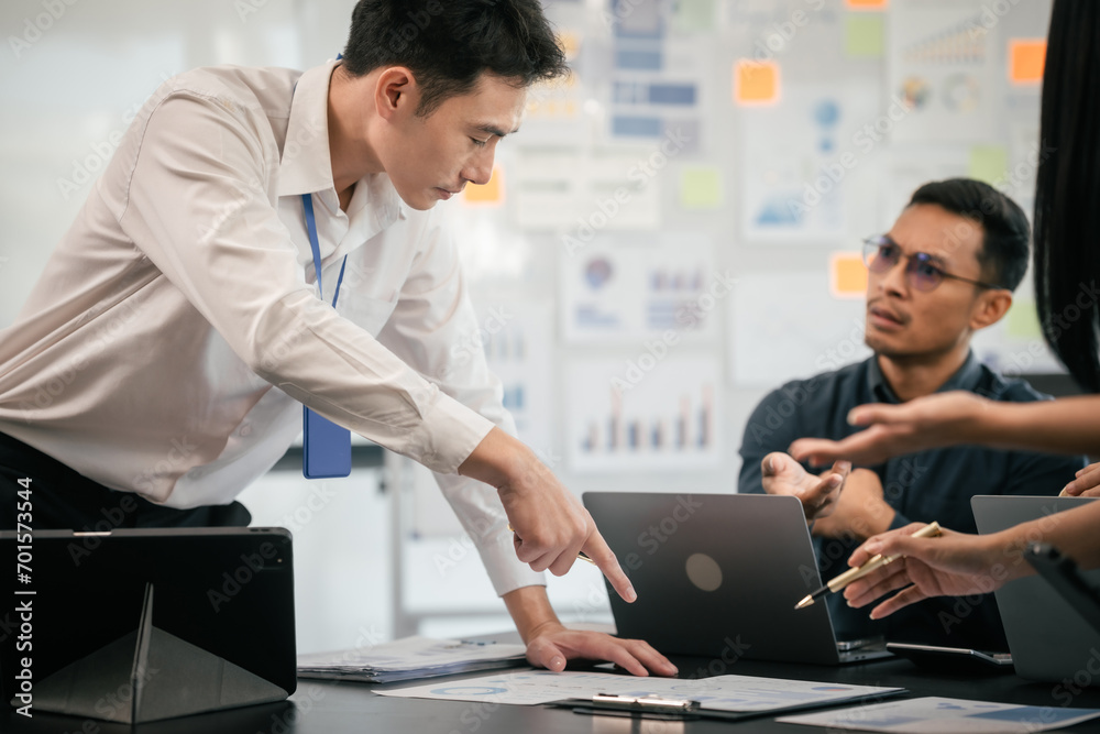 Fototapeta premium diverse group of Asian professionals, including middle-aged and mature individuals, gathered around a table in a business setting, discussing documents with focused attention.