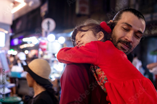Little girl in traditional Chinese clothing is tired from traveling and lies on her father's shoulder, Chinatown in the nighttime atmosphere, Chinese New Year holiday