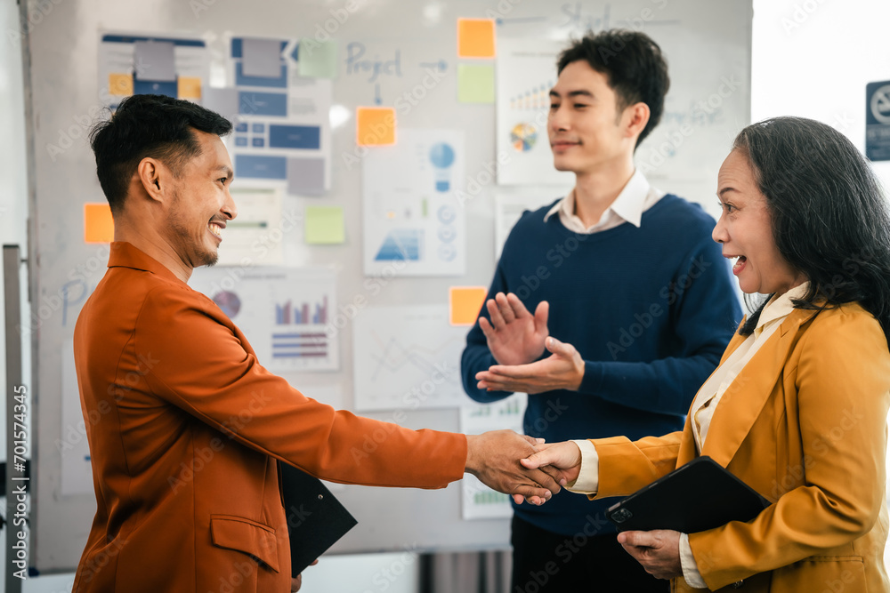Asian middle-age man and mature woman professionals engaged in boardroom meeting. presents data from clipboard to his colleagues, suggesting annual review or planning session. Asian middle-age man and mature woman professionals engaged in boardroom meeting. presents data from clipboard to his colleagues, suggesting annual review or planning session.