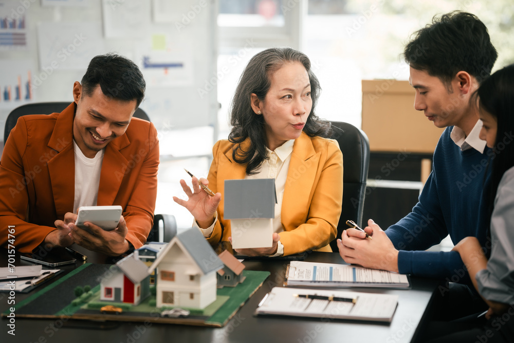 Fototapeta premium Asian real estate team engaged in a discussion, with two men and a woman focusing on a house model on a table, suggesting a planning or sales meeting.