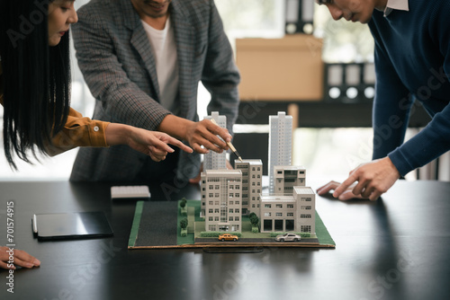 Asian team is engaged in a lively discussion over a scale model of a cityscape, likely representing a real estate or architectural project. photo