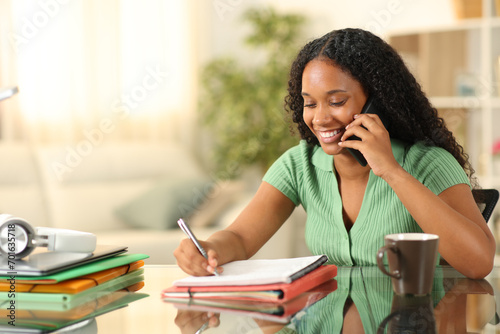 Black happy student calling on phone studying at home photo
