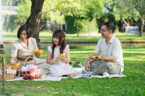 Happy family having picnic in the park with parents and kids sitting on the grass and enjoying healthy meals outdoors on a sunny summer day.